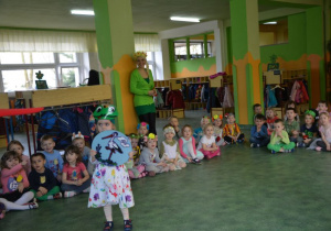 Dzieci siedzące dookoła sali i dziewczynka stojąca na środku z obrazkiem bociana