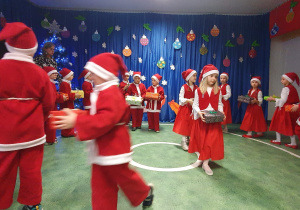Dzieci z grupy IX przebrane za Mikołajki i Mikołaje tańczą trzymając prezent w ręku.