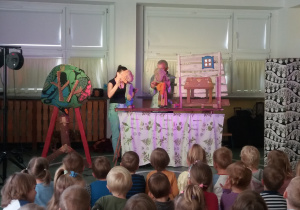 Aktorzy trzymają kukiełki chłopca i matki. W tle dekoracja drewnianego stołu i okna.