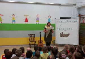 Pani Agatka trzyma w rękach ilustracje dwóch piesków. Na widowni siedzą dzieci.