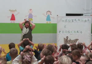 Pani Agatka i dzieci siedzące na widowni ilustrują piosenkę ruchem.