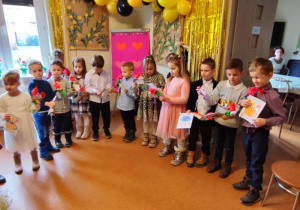 Dzieci trzymające laurki i kwiatki z papieru