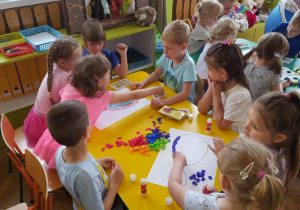 Dzieci siedzący przy stolikach wyklejają ilustrację balona kawałkami kolorowej bibuły.