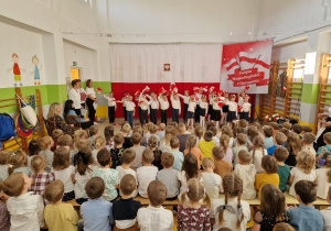 Dzieci machające biało-czerwonymi pomponami z bibuły podczas śpiewu
