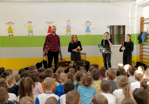 Dzieci siedzą na widowni i słuchają muzyków