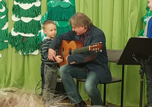 Mężczyzna pokazuje chłopcu sposób grania na gitarze.