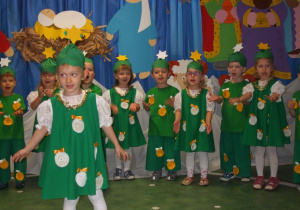 Dzieci przebrane za choinki ustawione w półkolu śpiewają piosenkę.