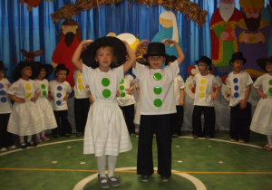 Dzieci przebrane za bałwanki śpiewają piosenkę, dwóch solistów stoi na środku trzymając ręce w górze.