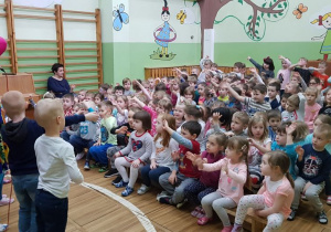 Dzieci siedzące na widowni naśladują ruchem rąk piosenkę śpiewaną przez Petronelę Zgiećśmieć..