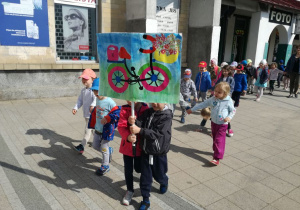 Dzieci spacerują w okolicy osiedla trzymając w dłoni przygotowane plakaty dotyczące ochrony środowiska.
