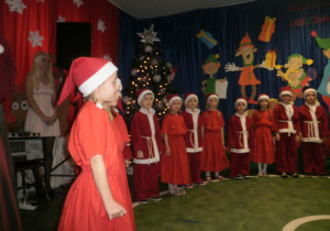 Dzieci przebrane za Mikołaje śpiewają piosenkę świąteczną.