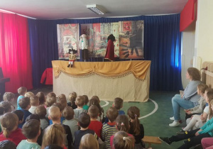 Dzieci na widowni oglądają scenkę przedstawiającą rozmowę medyka z księciem Brudasem w obecności syna Kocmołuszka.