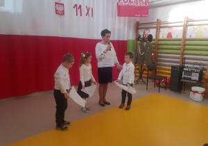 Dzieci trzymają rozcięty karton, a wychowawca opowiada przez mikrofon o rozbiorze Polski.