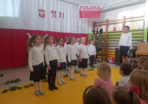 Dzieci w pozycji "Na baczność" śpiewają pieśń patriotyczną.