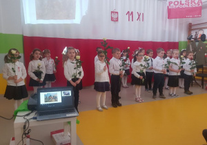 Dzieci trzymają w rękach biało-czerwone róże.