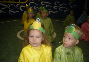 Dzieci przebrane za kolorowe bombki klęczą parami w rzędach, przygotowując się do występu.