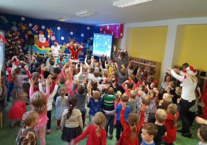 Dzieci, nauczyciele i prowadząca tańczą z uniesionymi rękami.
