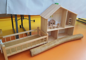 Zdjęcie przedstawia: duży domek z drewna, kołyskę i drewniany słupek.