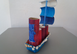 Statek wykonany przy użyciu papierowego pudełka, rurek po papierze toaletowym, niebieskiej słomki i muszelek.