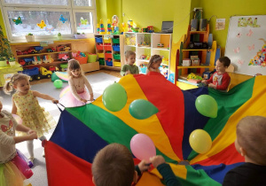 Dzieci z grupy II poruszają kolorowymi balonami umieszczonymi na chuście animacyjnej.