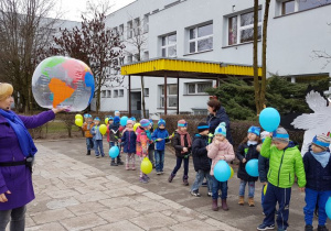 Pani Jola z piłką prezentującą kulę ziemską i dzieci z balonami wychodzące z przedszkola