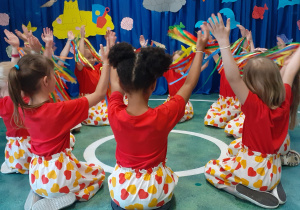 Dzieci z grupy VI tańczą w siadzie klęcznym unosząc kolorowe wstążki.